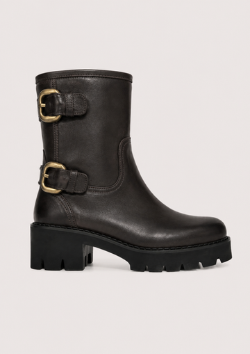 A black leather ankle boot with a chunky lug sole and two gold-tone buckle straps on the side, shown against a light gray background.