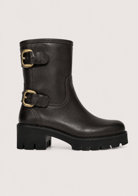 A black leather ankle boot with a chunky lug sole and two gold-tone buckle straps on the side, shown against a light gray background.