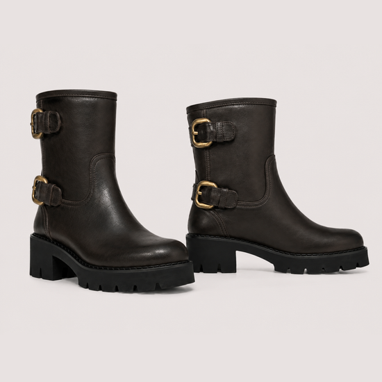 A pair of dark brown leather ankle boots with chunky black block heels and gold-tone buckle straps, shown against a light gray studio background.