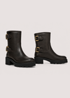 A pair of dark brown leather ankle boots with chunky black block heels and gold-tone buckle straps, shown against a light gray studio background.