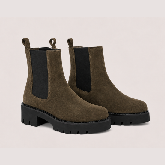 A Khaki suede Chelsea boot with a chunky black sole and a black elastic side panel, shown from a side profile on a light beige background.