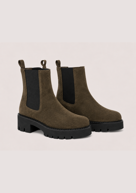 A Khaki suede Chelsea boot with a chunky black sole and a black elastic side panel, shown from a side profile on a light beige background.