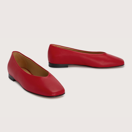 Pair of red leather flat shoes on a light gray background