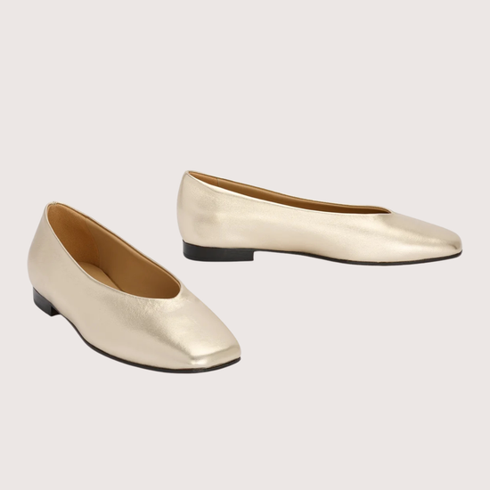 Pair of gold flat shoes on a light beige background