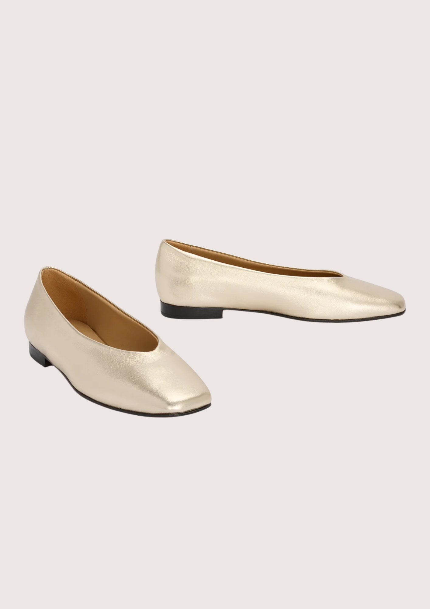 Pair of gold flat shoes on a light beige background