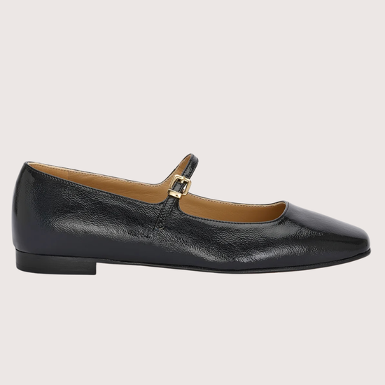 Black leather flat shoe with a gold buckle on a light gray background