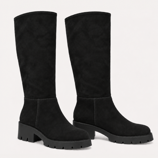 A pair of black knee-high suede boots with chunky lug soles and block heels, shown against a plain off-white background.