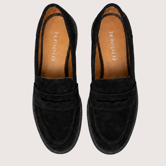 Black suede loafer on a plain grey background.