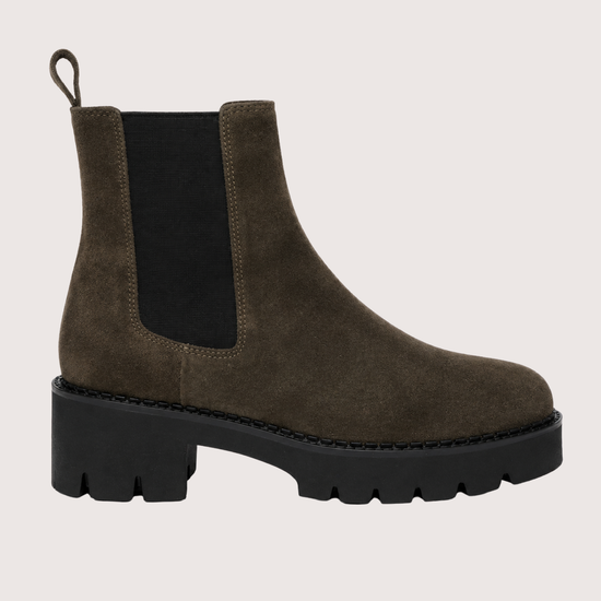A Khaki suede Chelsea boot with a chunky black sole and a black elastic side panel, shown from a side profile on a light beige background.