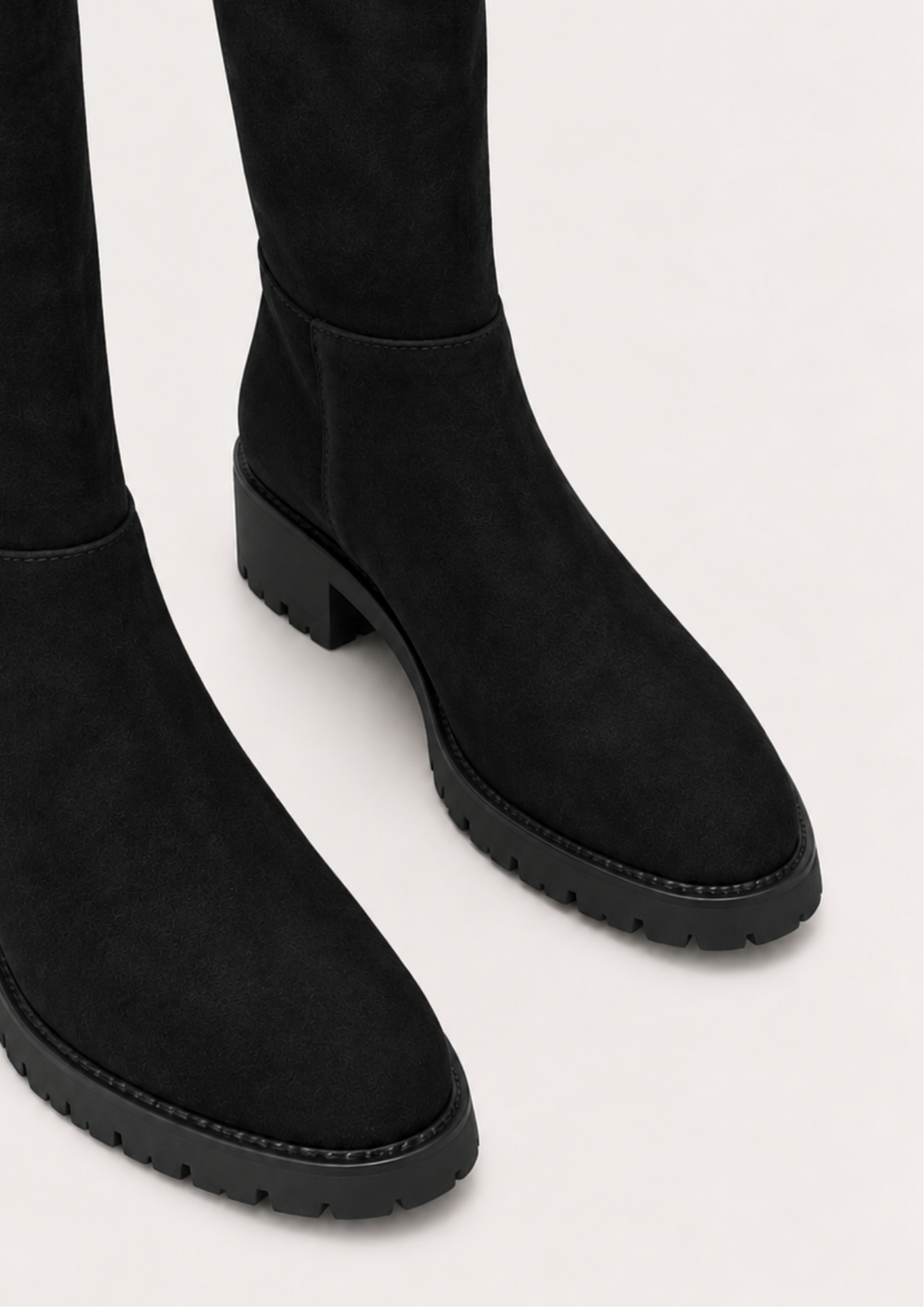 Black suede over-the-knee boots with chunky lug soles, shown from a close-up angle on a light gray background.