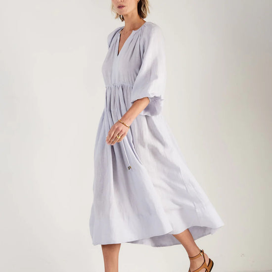 Woman wearing a light blue dress by Mondo Corsini on a white background. Side view