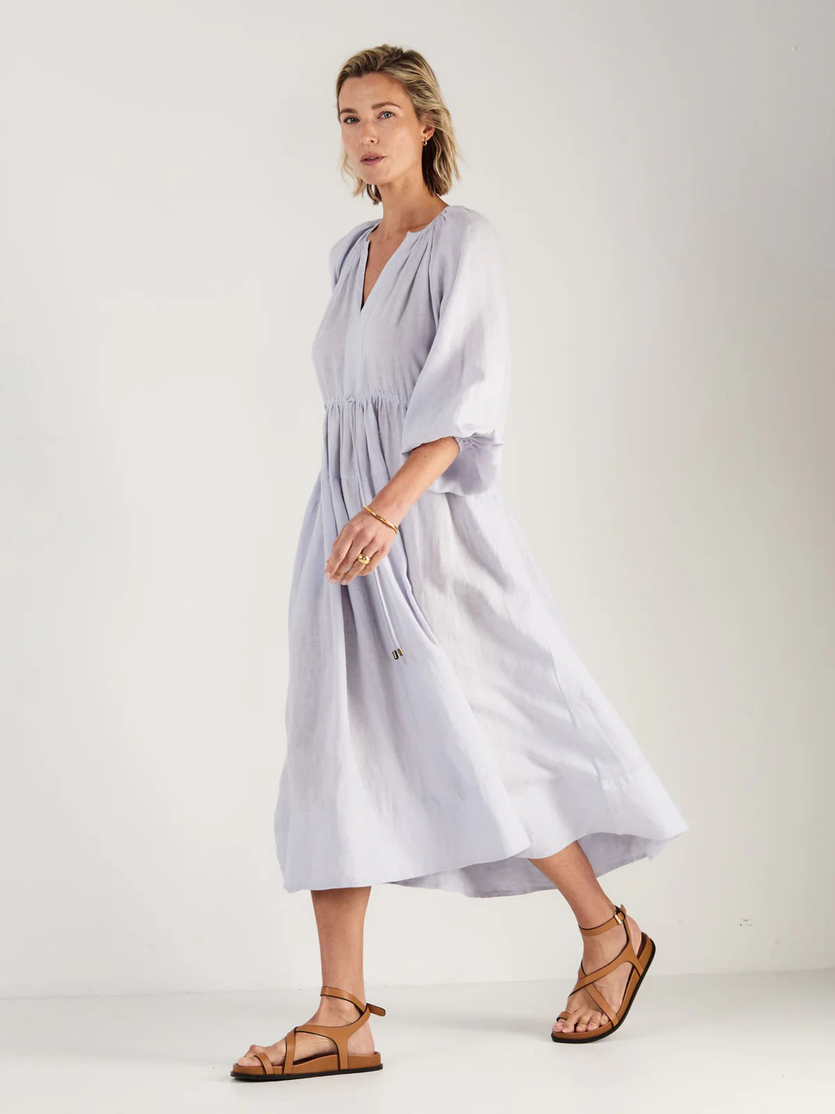 Woman wearing a light blue dress by Mondo Corsini on a white background. Side view