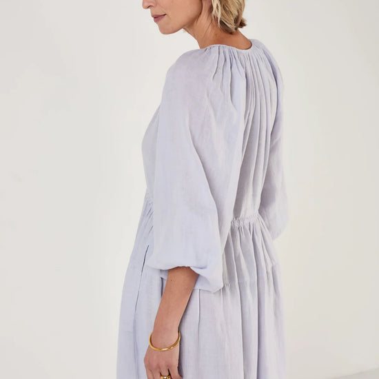 Woman wearing a light blue dress by Mondo Corsini on a white background. Side view close up