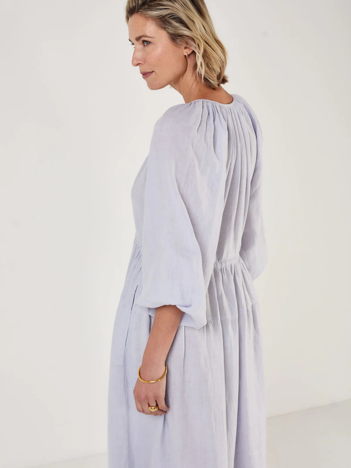 Woman wearing a light blue dress by Mondo Corsini on a white background. Side view close up
