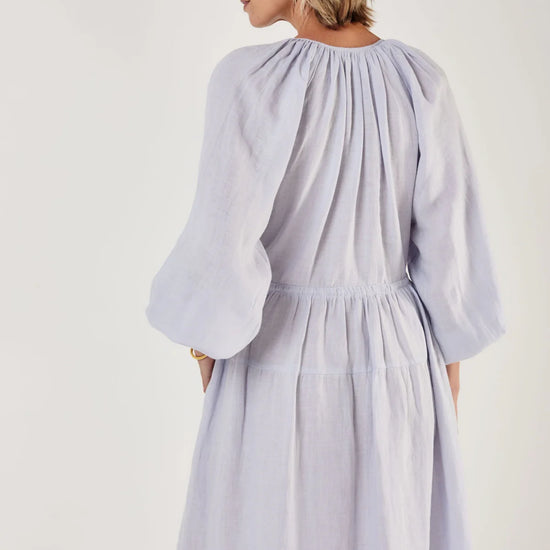 Woman wearing a light blue dress by Mondo Corsini on a white background. Rear view