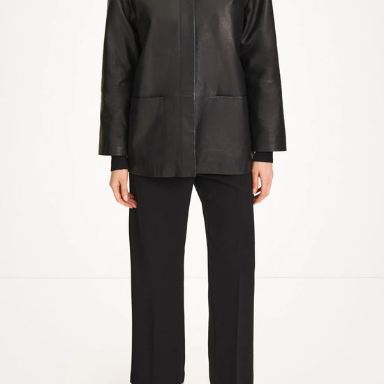 A model wearing a black leather jacket with a mock neck, black wide-leg cropped trousers, and black pointed-toe heels, photographed against a seamless white studio background.