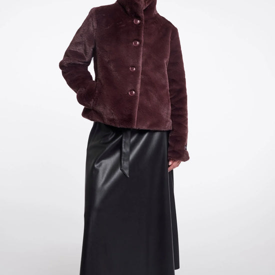 Woman wearing a brown textured jacket and black leather skirt on a white background