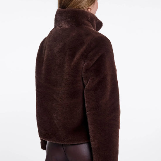 A model shown from the back wearing a dark brown plush faux fur jacket and dark brown pants against a plain white studio background.