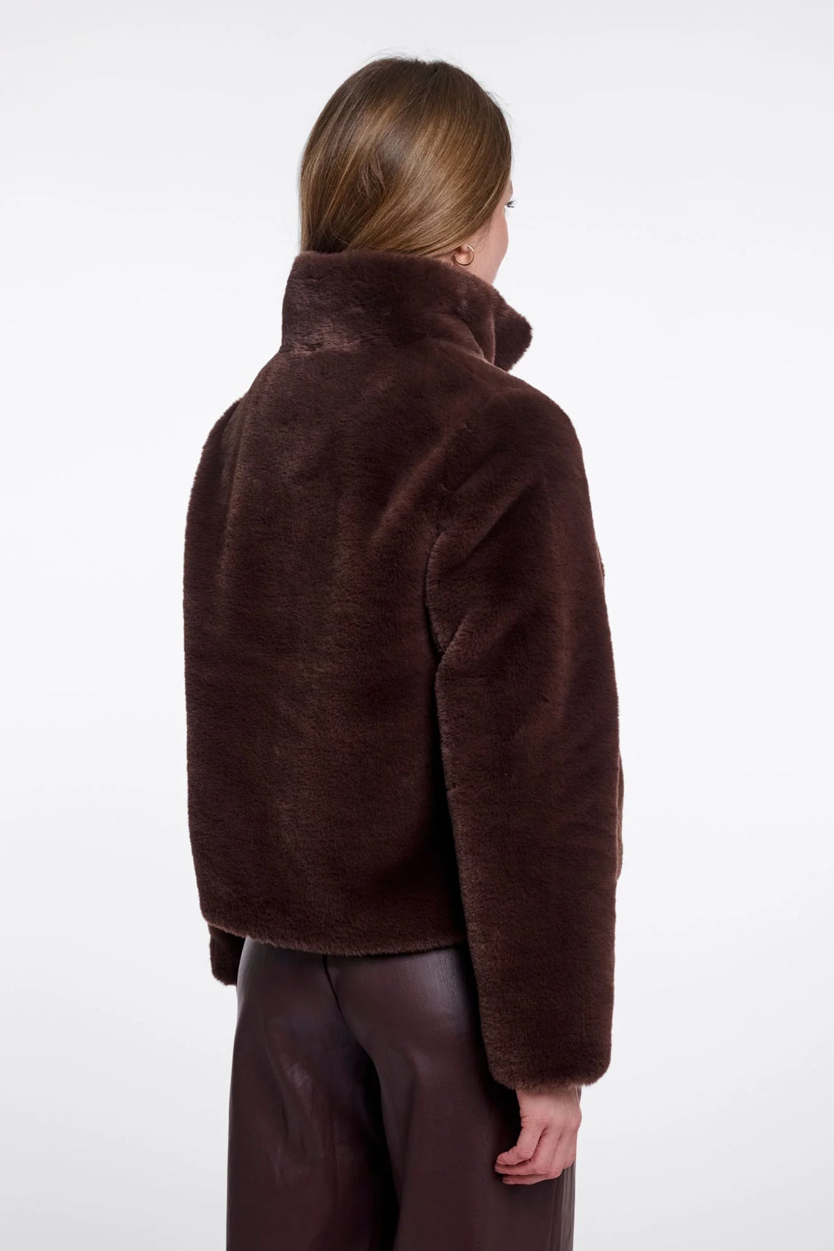 A model shown from the back wearing a dark brown plush faux fur jacket and dark brown pants against a plain white studio background.