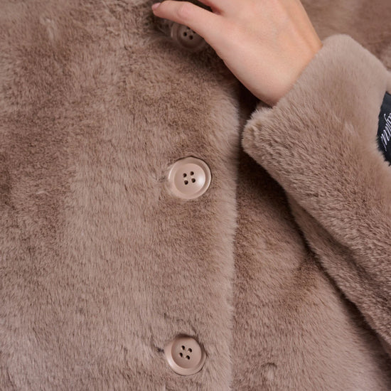 Close-up of a brown fluffy coat with buttons and a hand touching the fabric.