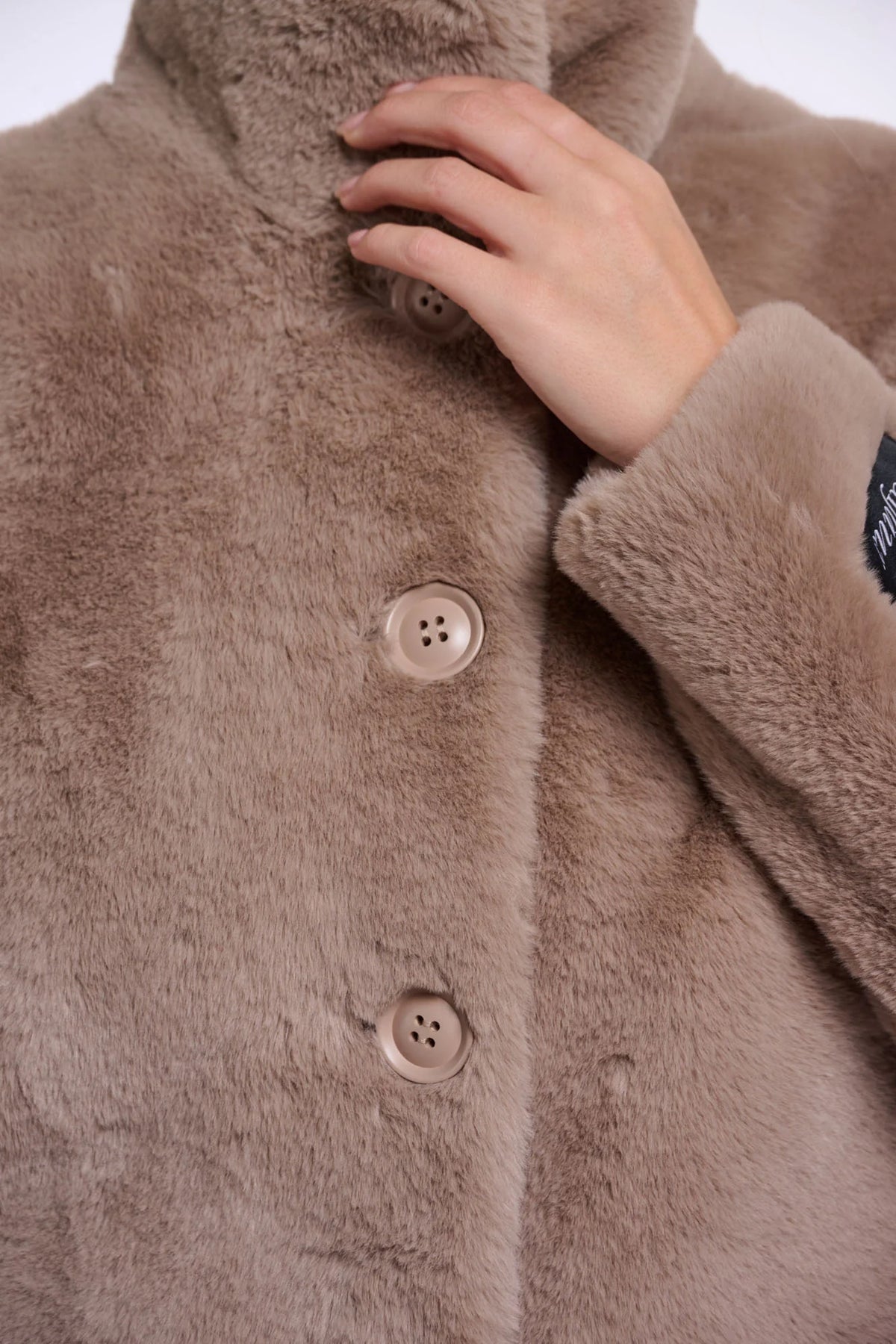 Close-up of a brown fluffy coat with buttons and a hand touching the fabric.