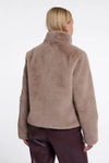 A woman viewed from the back wearing a soft, fuzzy cropped jacket in a taupe-brown color, paired with dark brown pants, against a plain white studio background.