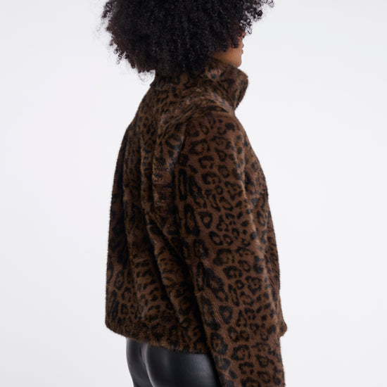 A person shown from the back wearing a brown and black leopard-print faux-fur jacket and black pants against a plain light gray studio background.