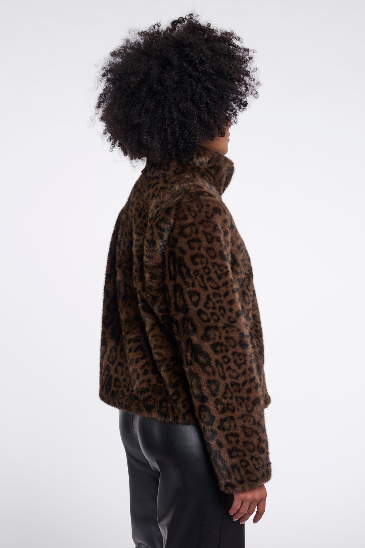 A person shown from the back wearing a brown and black leopard-print faux-fur jacket and black pants against a plain light gray studio background.