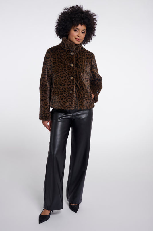 A model wearing a brown and black leopard-print faux fur jacket with a high collar, paired with black faux leather wide-leg pants and black pointed-toe heels, photographed against a light gray studio background.