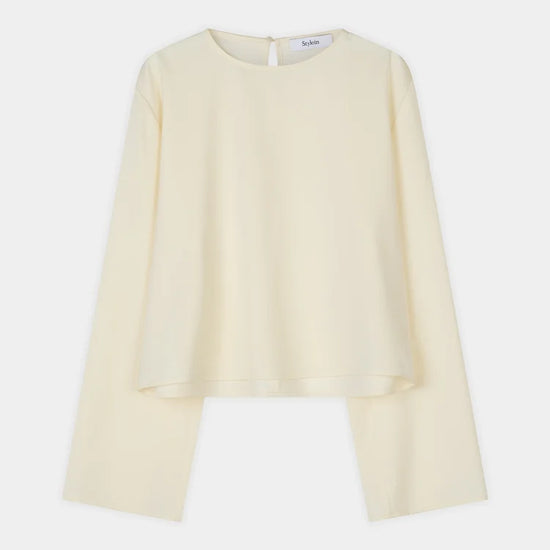 A pale cream long-sleeve blouse with a round neckline and a unique asymmetrical hemline, displayed flat against a light gray background.