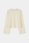 A pale cream long-sleeve blouse with a round neckline and a unique asymmetrical hemline, displayed flat against a light gray background.