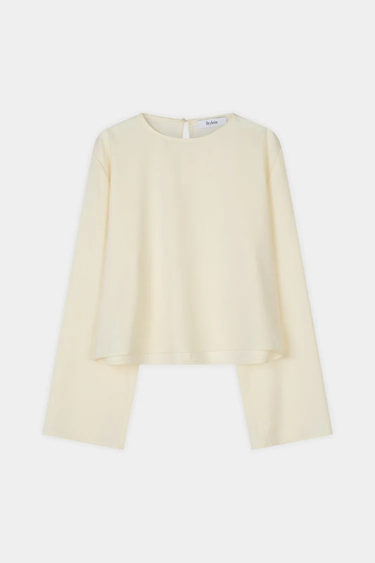 A pale cream long-sleeve blouse with a round neckline and a unique asymmetrical hemline, displayed flat against a light gray background.