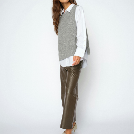 A woman modeling a gray knit sweater vest over a white collared shirt, paired with brown leather cropped pants and beige pointed-toe heels, against a light gray studio background.