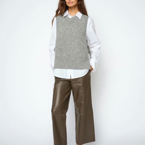 A woman modeling a gray knit sweater vest over a white collared shirt, paired with brown wide-leg cropped pants and beige pointed-toe heels, against a light gray studio background.