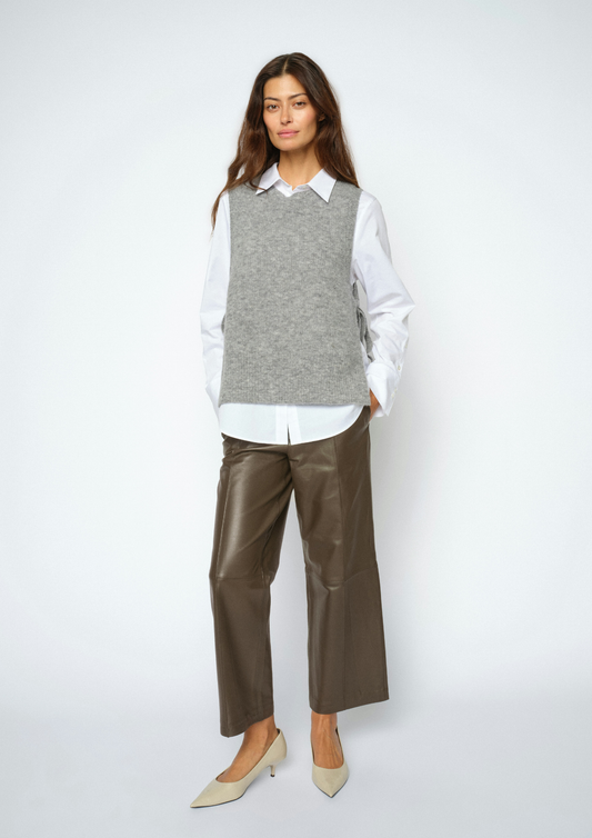 A woman modeling a gray knit sweater vest over a white collared shirt, paired with brown wide-leg cropped pants and beige pointed-toe heels, against a light gray studio background.