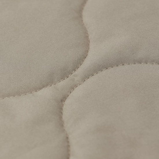 Close-up of a quilted fabric surface in a warm light beige or oatmeal tone, showing stitched oval sections and soft texture.