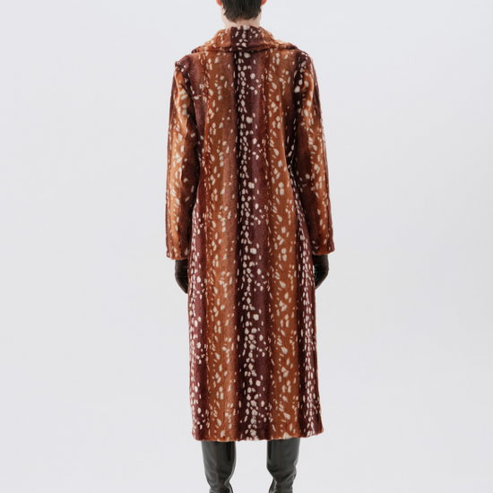 A model viewed from the back wearing a long brown coat with a white floral pattern, paired with dark gray pants and brown boots, set against a plain light gray studio background.