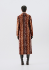 A model viewed from the back wearing a long brown coat with a white floral pattern, paired with dark gray pants and brown boots, set against a plain light gray studio background.