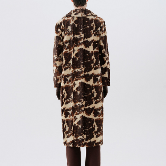 A model viewed from the back wearing a long brown and beige animal-print faux fur coat, paired with dark brown trousers and black shoes, against a light gray studio background.