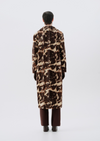 A model viewed from the back wearing a long brown and beige animal-print faux fur coat, paired with dark brown trousers and black shoes, against a light gray studio background.