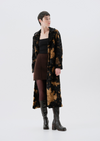 Person wearing a long, patterned coat over a black top and brown skirt on a white background