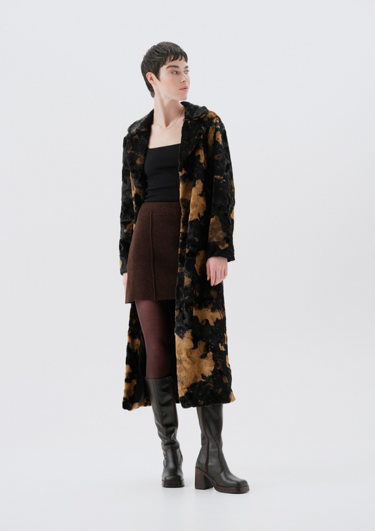 Person wearing a long, patterned coat over a black top and brown skirt on a white background