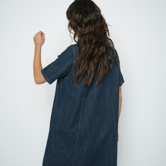 A child wearing a dark blue denim short-sleeve dress, shown from the back against a plain white studio background.