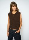 A woman modeling a sleeveless, crew-neck knit vest in a dark brown color, paired with dark blue jeans, against a plain light gray background. 