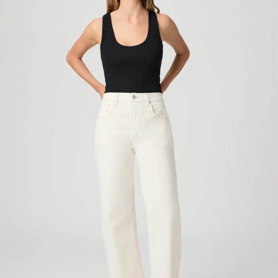 Woman wearing a black tank top and white Paige Jeans on a plain background