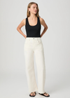Woman wearing a black tank top and white Paige Jeans on a plain background