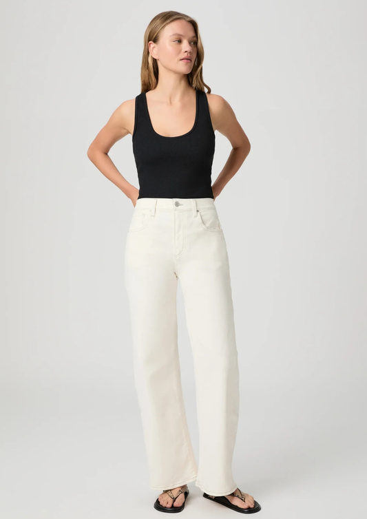 Woman wearing a black tank top and white Paige Jeans on a plain background