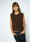 A woman modeling a sleeveless, crew-neck knit vest in a dark brown color, paired with dark blue jeans, against a plain light gray background.