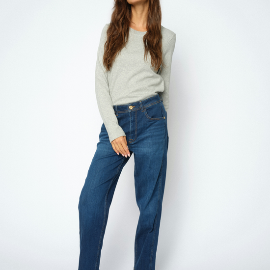 A woman modeling a light gray long-sleeve knit sweater, dark blue straight-leg jeans, and black pointed-toe slingback heels against a plain light gray studio background.