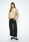 A woman modeling a shiny champagne-gold satin bomber jacket paired with black wide-leg trousers and black loafers, standing against a plain white studio background.